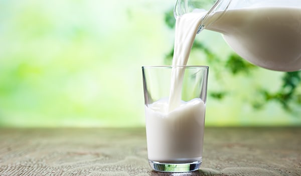 Pitcher pouring milk into a glass on a table.