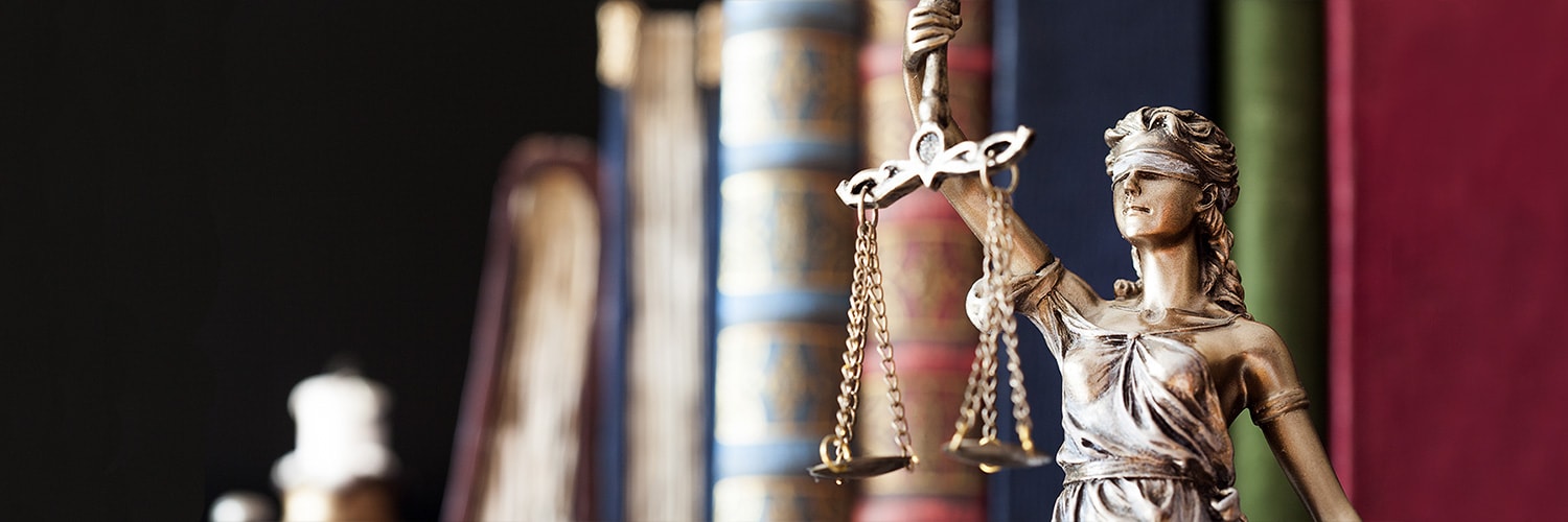 Lady justice statue holding scales with books in the background