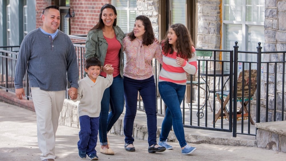 Family of five walking on sidewalk in front of houses.