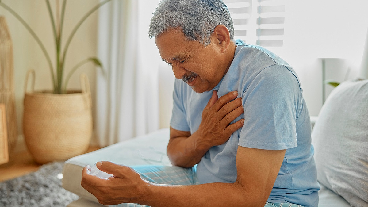 Older man sitting up in bed, wincing and holding his heart and/or shoulder in pain.