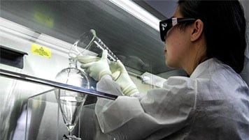 A scientist pours liquid from one flask to another as part of wastewater testing for poliovirus.