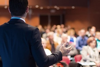 Image of a conference with speaker and participants.