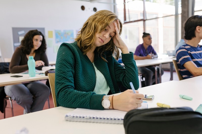 Tired high school student sitting in a classroom and writing on a notepad