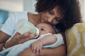 Mother feeding infant baby a bottle, while cradling infant in her arms.