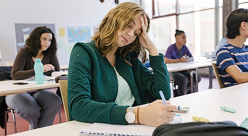 Unhappy, White, female student, studying in class with head in hand.