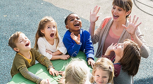 Several young, elementary school children and teacher being silly on a playground.