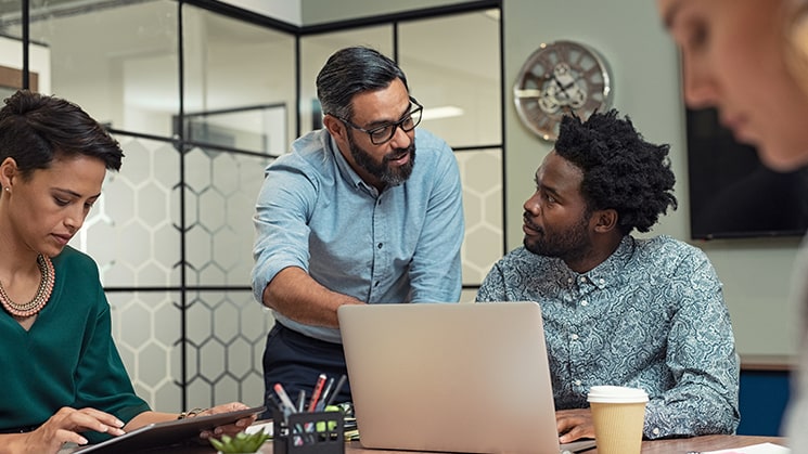 Two women and two men sitting around an office table working together. Two of them are discussing what is on an open laptop.