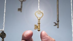 A golden key that is hanging by a thread. It is about to be grabbed with a thumb and index finger.