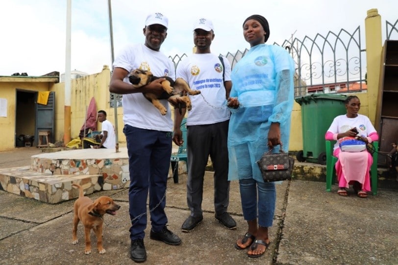 three people stand together, one holding a dog and there is another dog at their feet