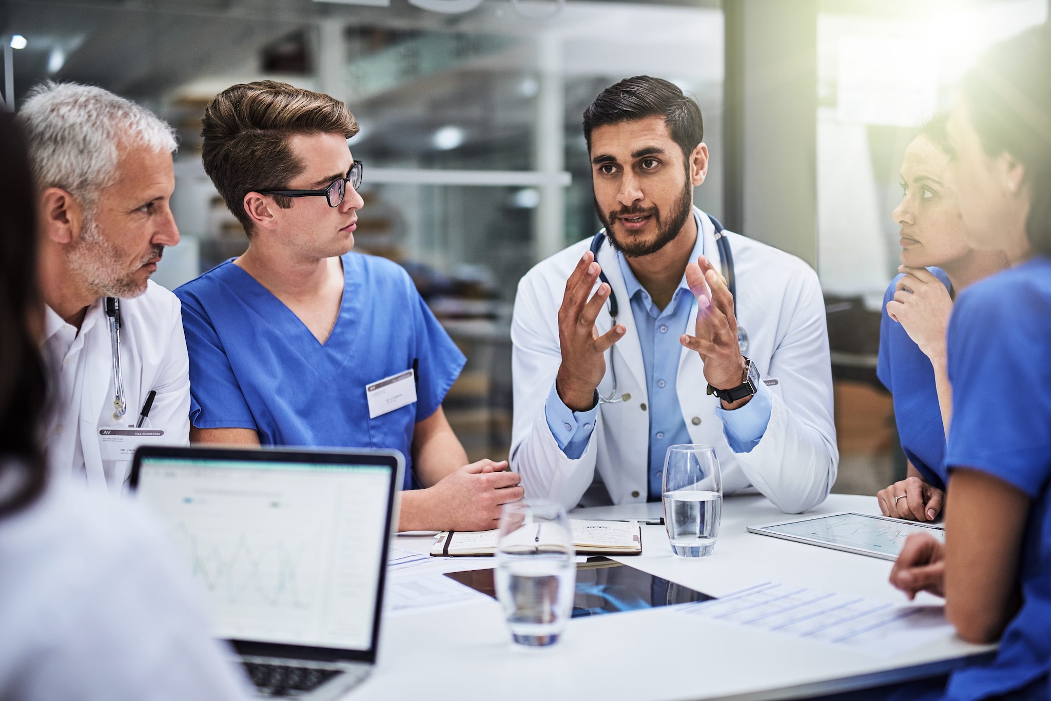 A doctor addresses a team of healthcare professionals around a table