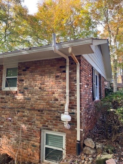 Corner view of a brick home with a pipe coming out of the side wall and up over the gutter to release radon into the air above the home.