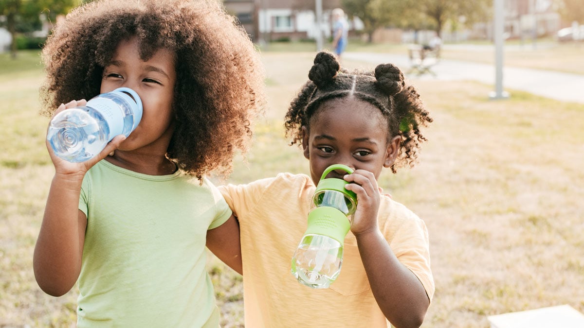 Two girls at a park drinking water from their water bottles