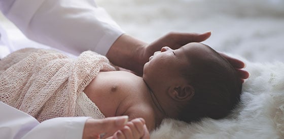 Sleeping baby lying in bed, with mother holding baby's face