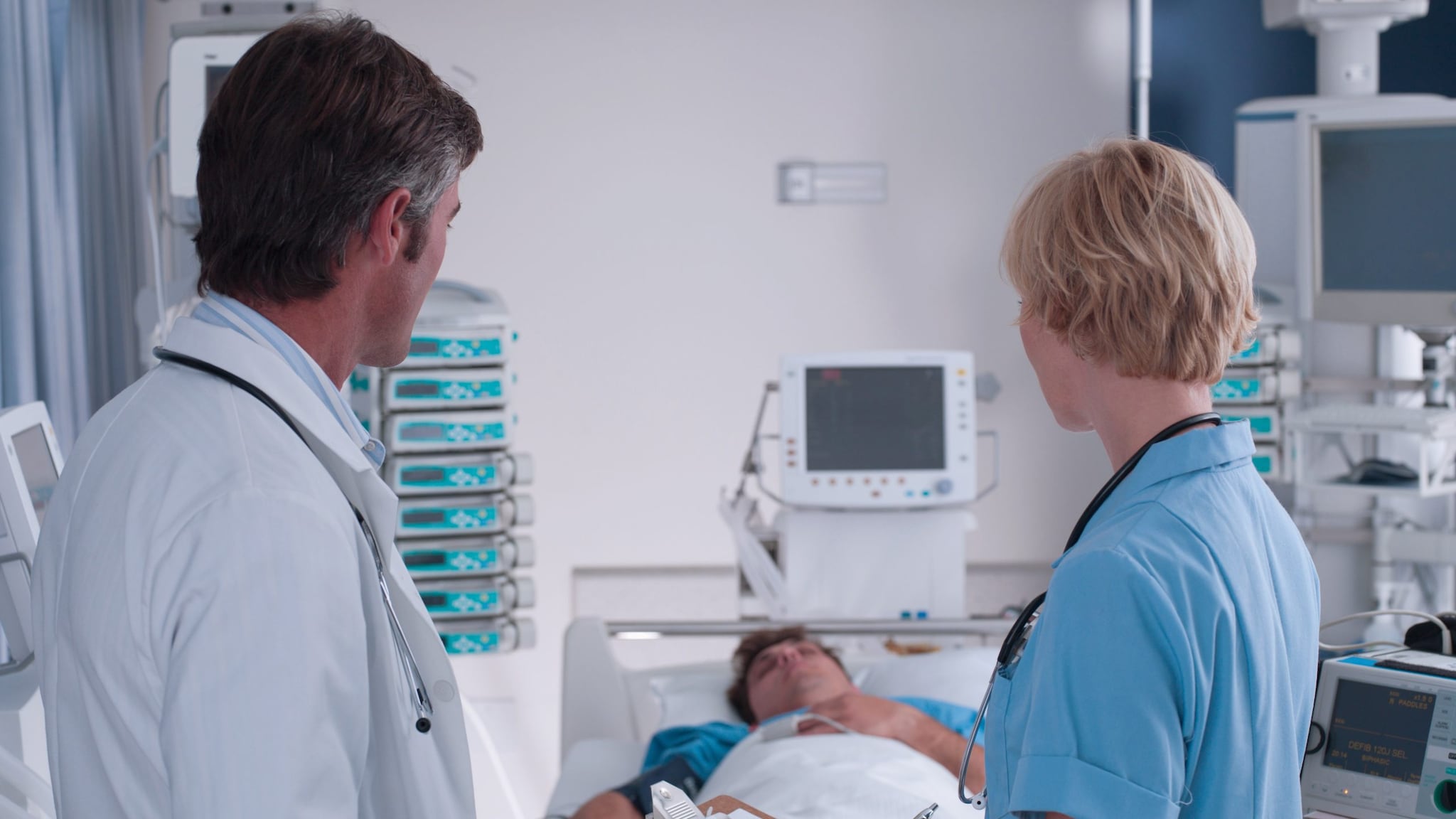 Doctor and nurse talking in presence of a patient lying in bed.