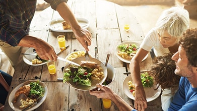 Two people sitting at a wooden table being served food by another person who is standing.