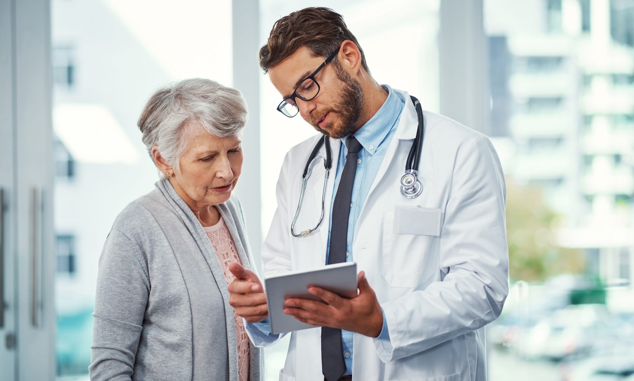 A doctor holding a clipboard speaking to an older patient. Both doctor and patient are looking at the clipboard.