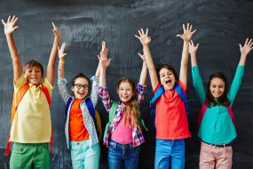 Students in front of a chalk board smiling and happy with their arms raised over their heads.