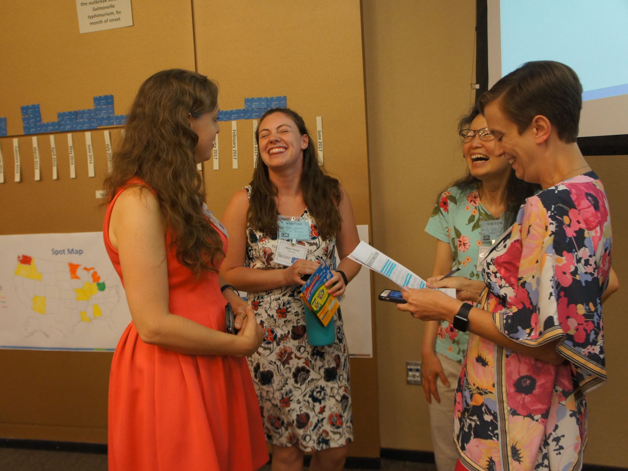 A group of female teachers dressed in colorful attire laughing and loving their jobs in a classroom setting.