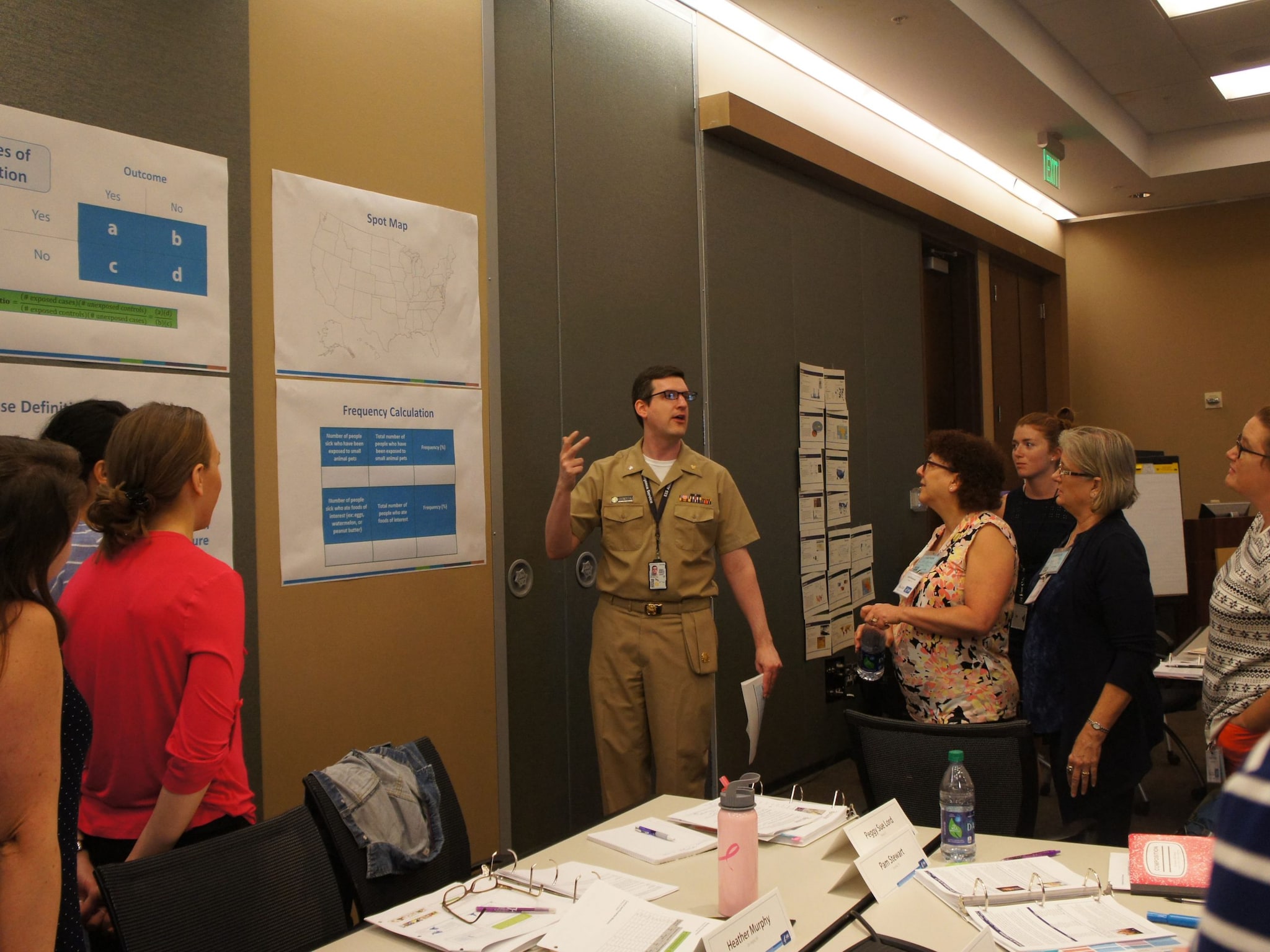 A man presents information on posters hanging on the walls to a group of female teachers in a classroom setting.