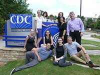 A teacher and students pose around a CDC sign on a grassy hill.