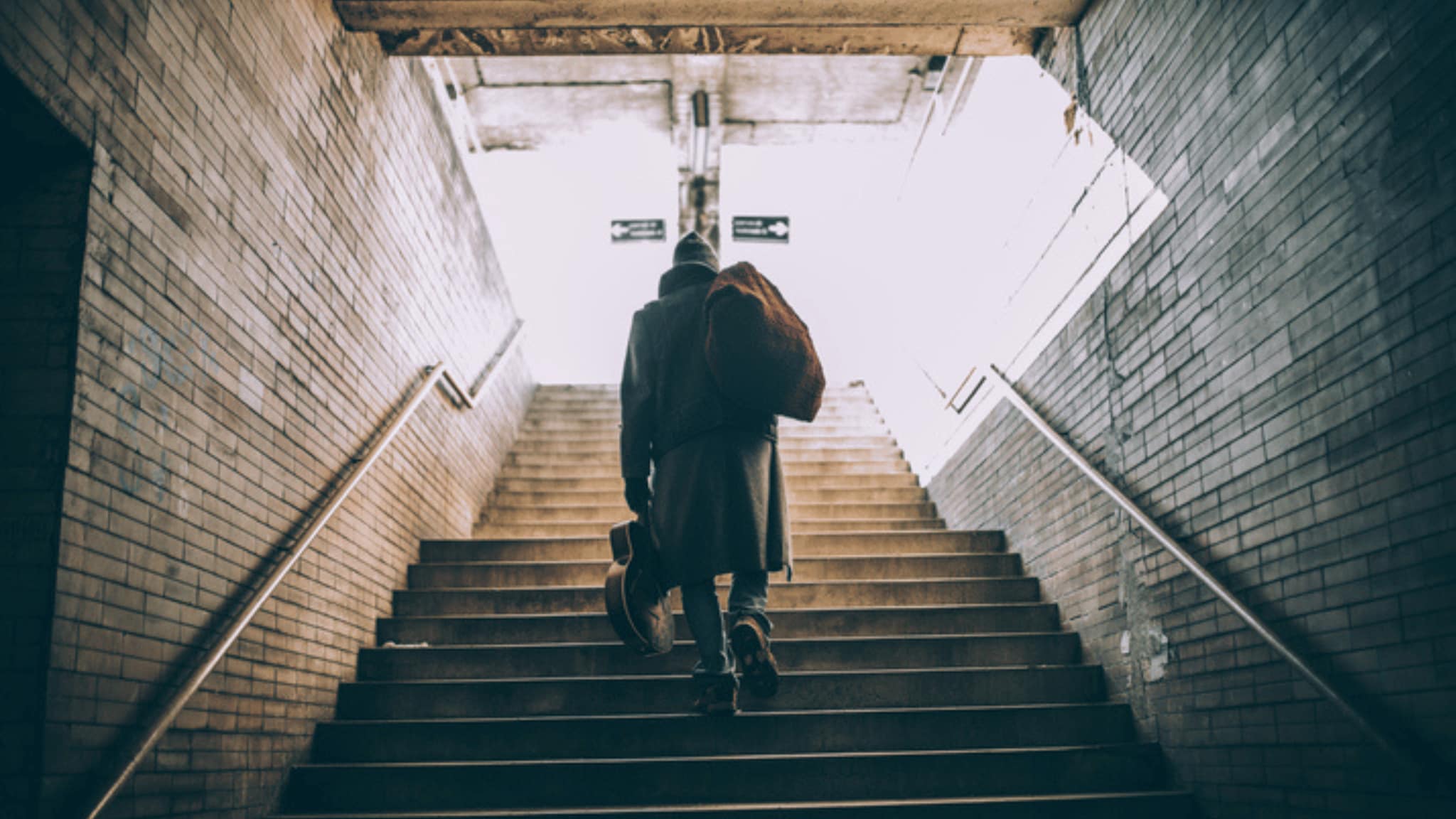 Man holding bag and guitar walking up stairs