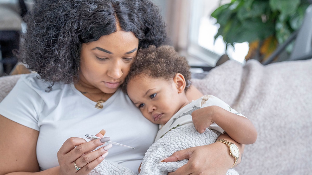 Mom reading thermometer while holding toddler.