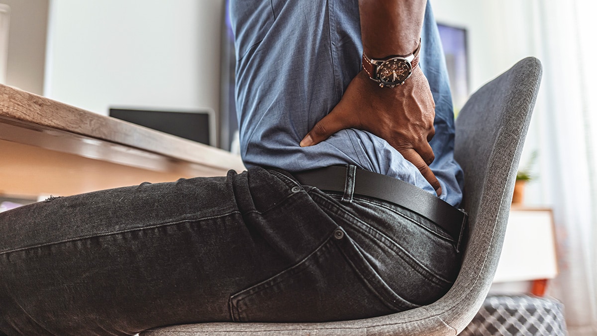 Man sitting in a desk chair with his hands on his back