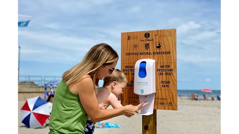 Terri Flori ayuda a su hijo Kai a aplicarse protector solar de un dispensador de Scarborough State Beach en Narragansett, Rhode Island.