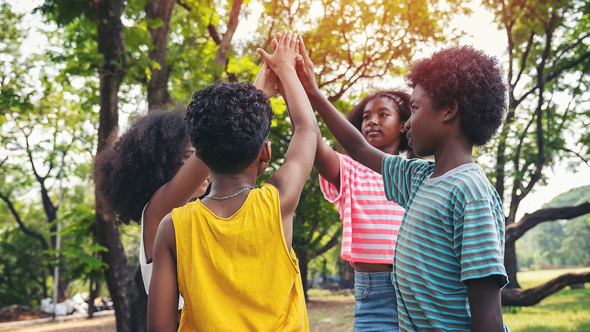 Schoolkids outdoors in a circle, hands raised together in the middle.