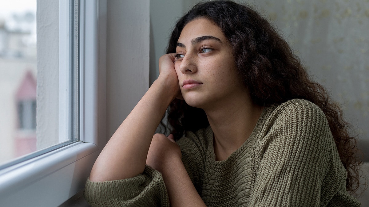 Young, sad woman looking out a window.