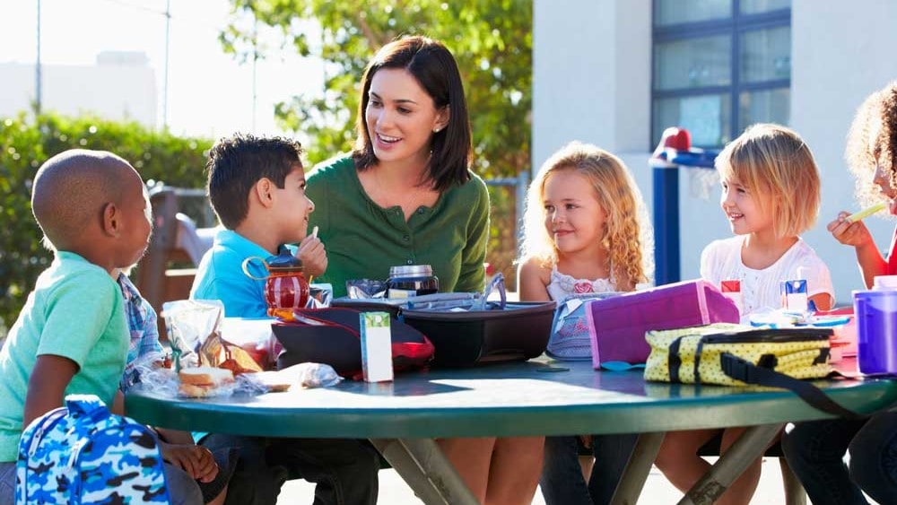 Woman sitting at picnic table with four young children.