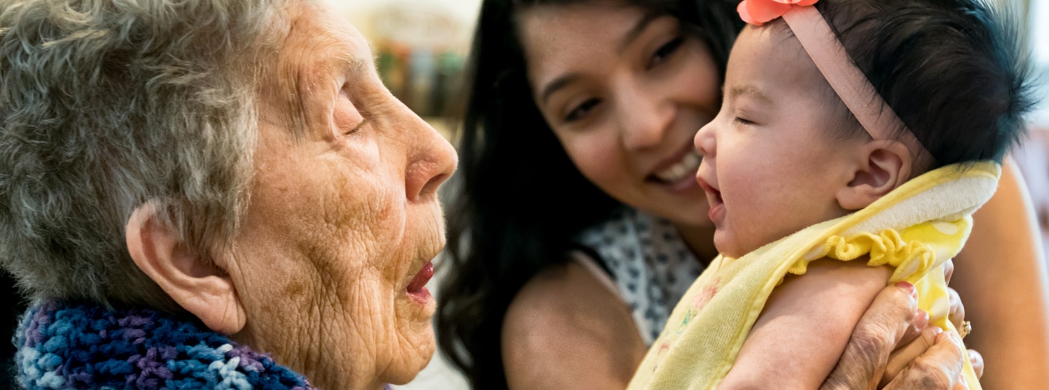 Abuela con su nieta alzando la biznieta y sonriendo.