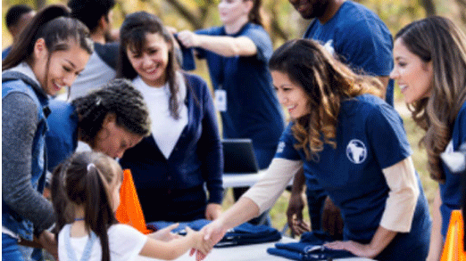 a woman surrounded by other women volunteering at a table and shaking hands with a little girl