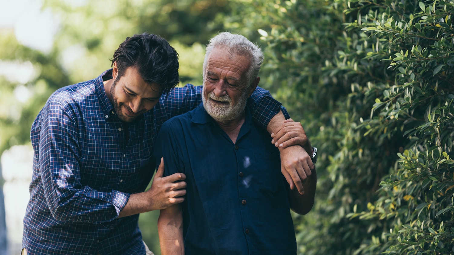 The old man and his son are walking in the park. A man hugs…