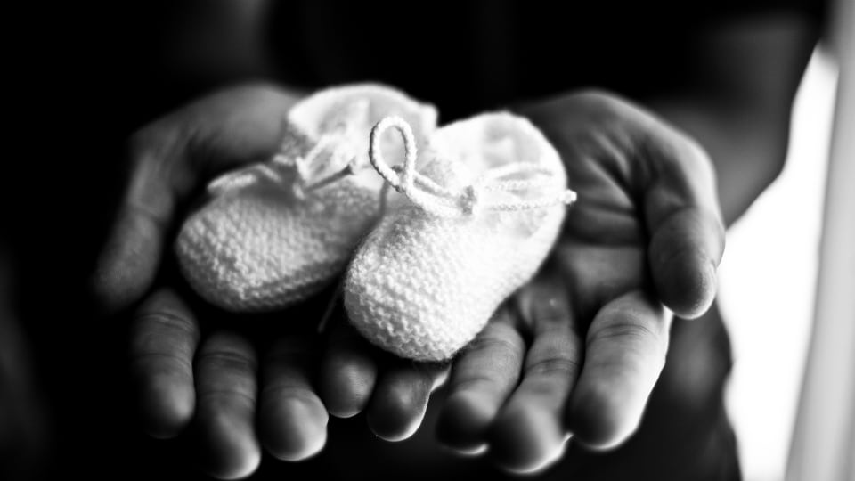 Black and white photo of adult hands holding baby shoes