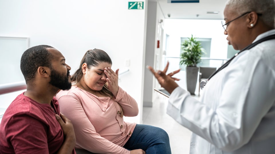 Female doctor talking to sad couple in a hospital.