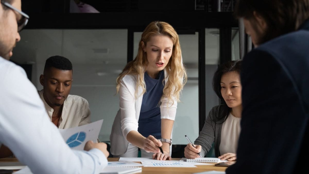 A woman explaining graphs to four coworkers in a meeting room.