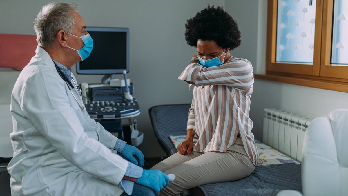 A health care provider observes a patient coughing during a medical exam.