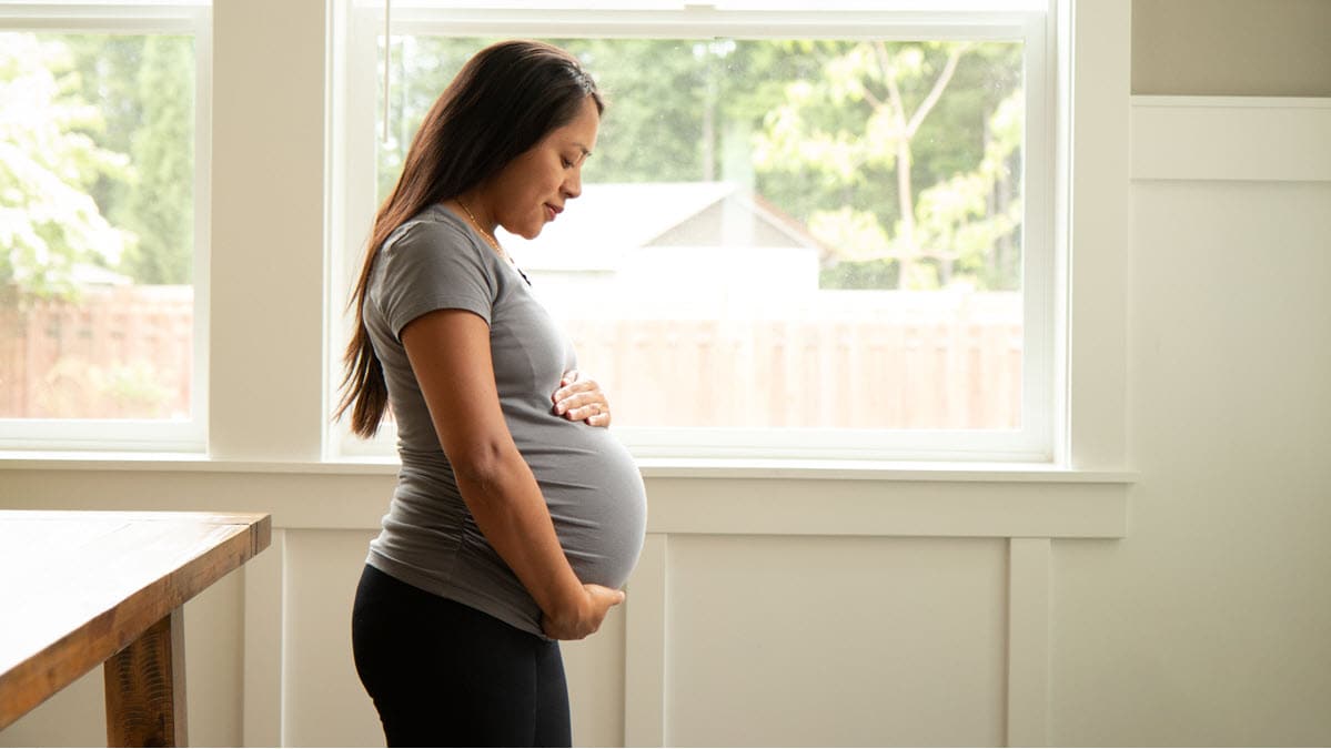 Young pregnant Hispanic woman looking at her belly