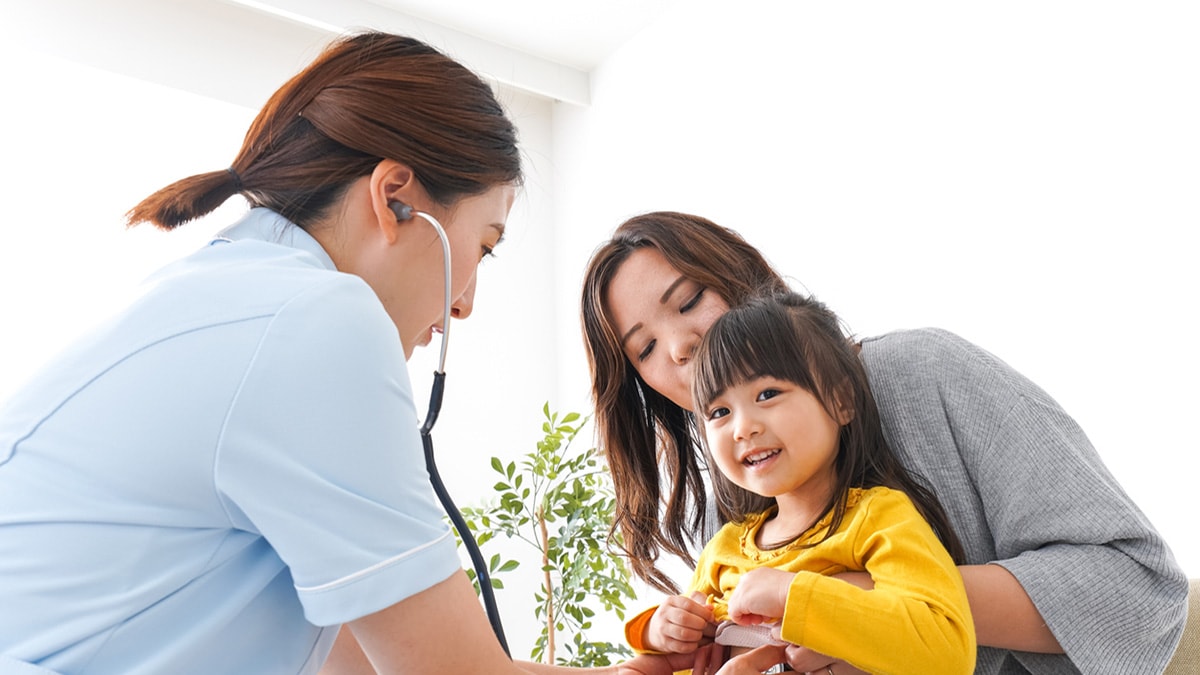 Mother holding daughter on lap while doctor listens to the child's heartbeat