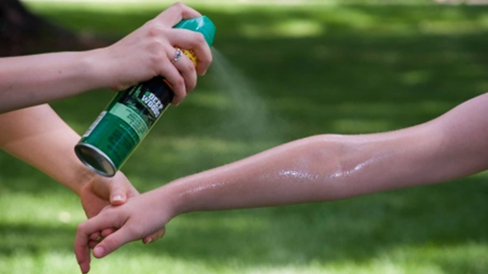 Person spraying insect repellent on another's arm