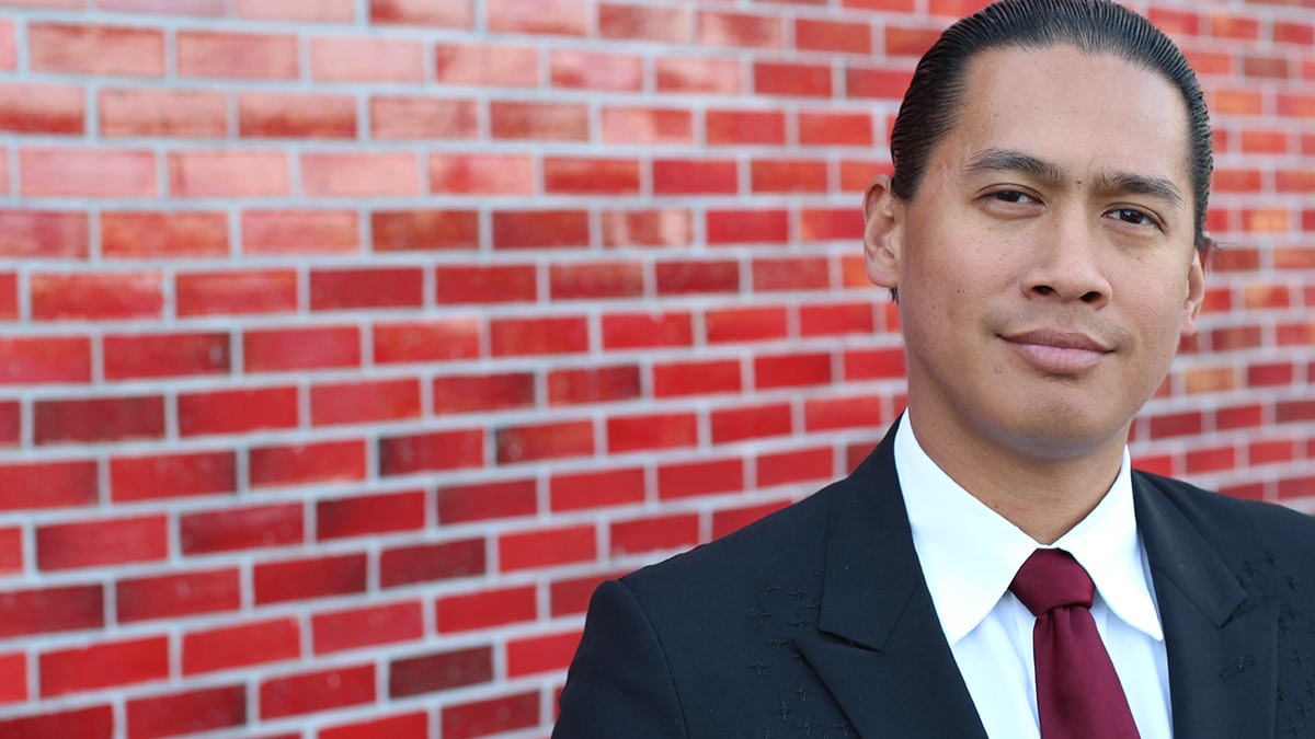 A young man in a suit in front of a brick wall