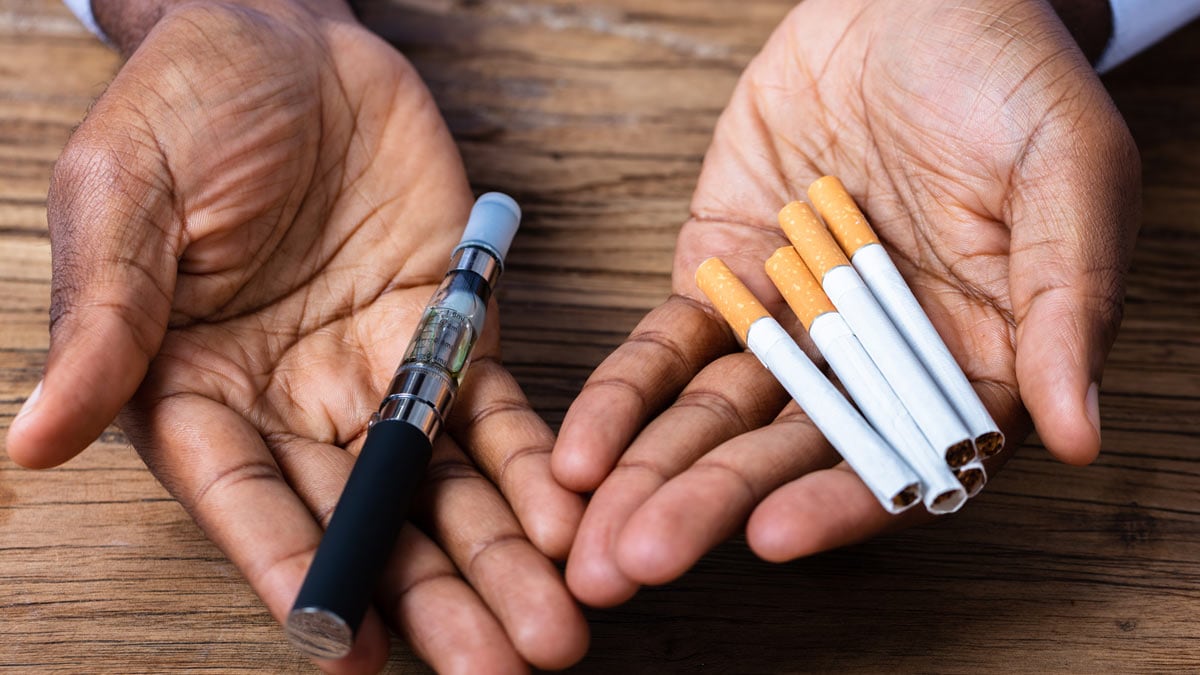 Hands holding cigarettes and a vape