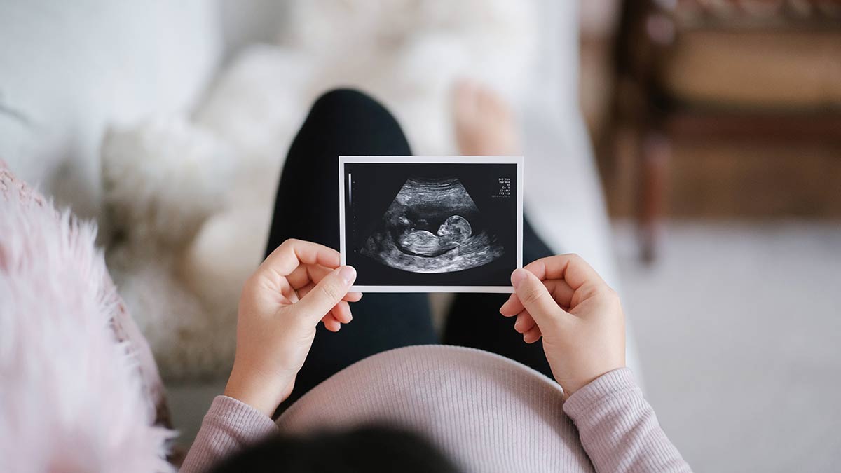 Pregnant woman lying on sofa at home looking at the ultrasound scan photo of her baby