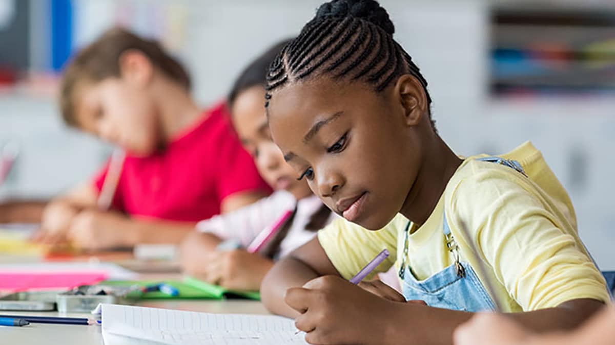 Niños en la escuela sentados en sus escritorios escribiendo.