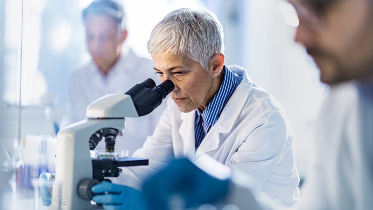 Senior female scientist working on a microscope among her colleagues in laboratory.