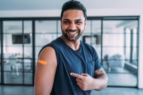 A young man smiling and pointing to his arm after getting his shot.