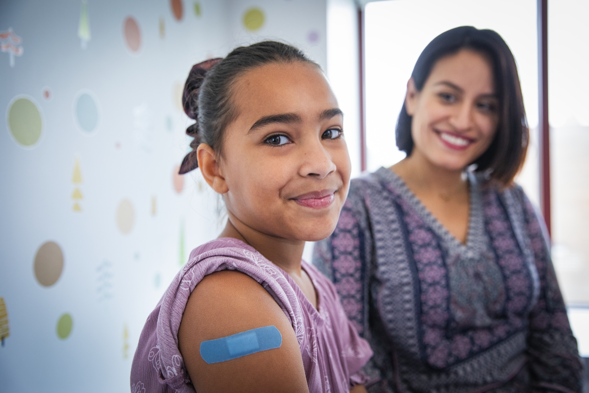 Pediatric Patient smiling with parent at doctor's office with band aid on upper arm.