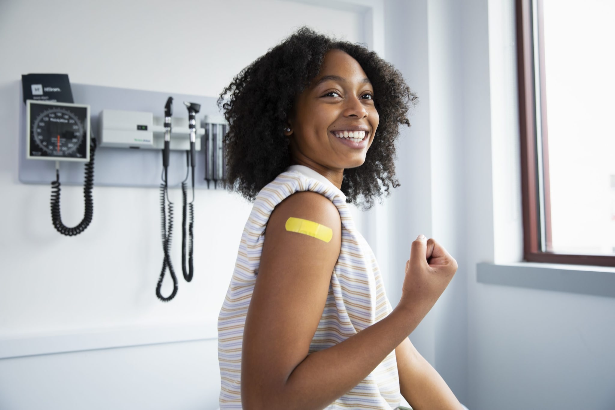 Adolescent Patient smiling with Bandaid on upper arm post vaccination.