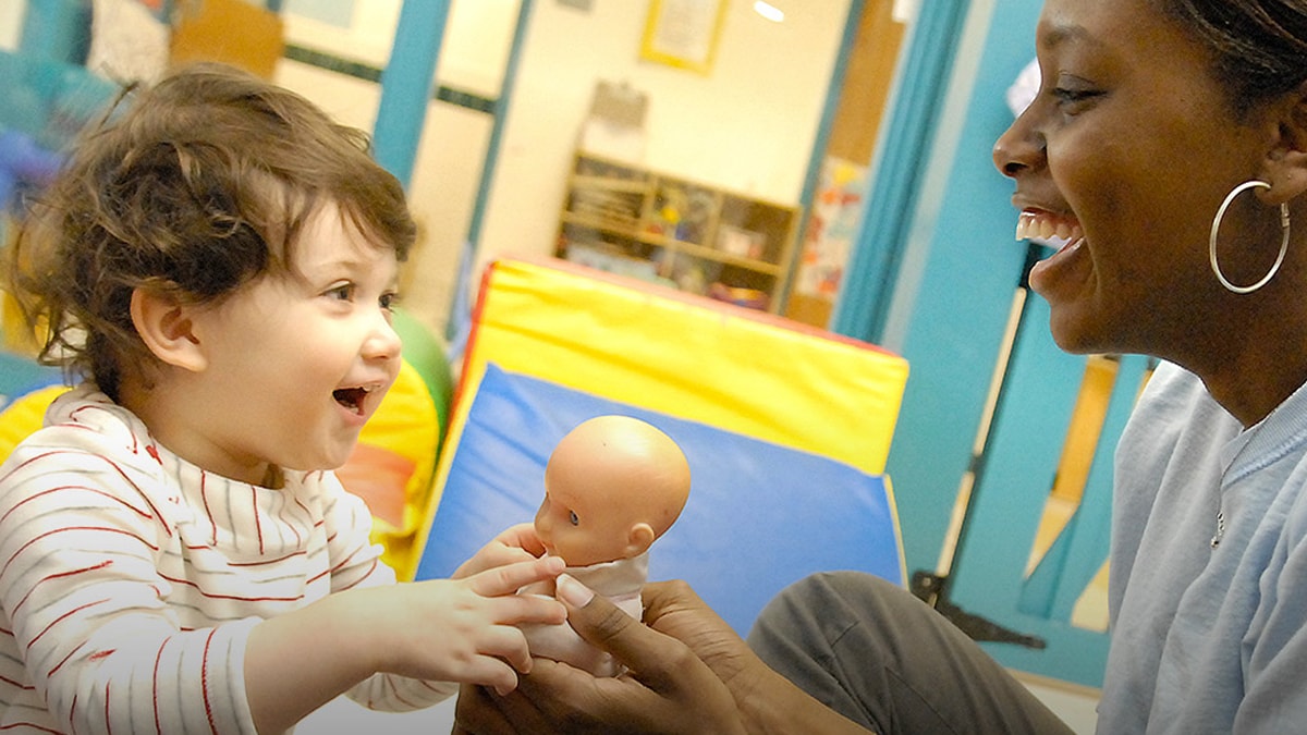 Teacher playing with child and baby doll